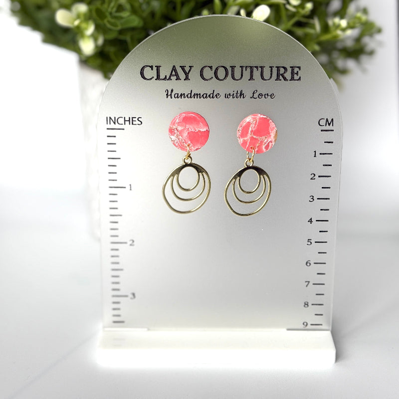 Polymer clay marbled earrings in blush color with resin finish and brass charms on a 'Clay Couture' branded size stand