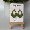Polymer clay earrings in olive grove color with brass connectors and 18K gold plated studs  on a 'Clay Couture' branded card with a wooden stand
