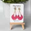 Pink clay earrings on a 'Clay Couture' branded card with a wooden stand.
