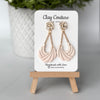Pair of champaigne earrings on a 'Clay Couture' branded card with a wooden stand.