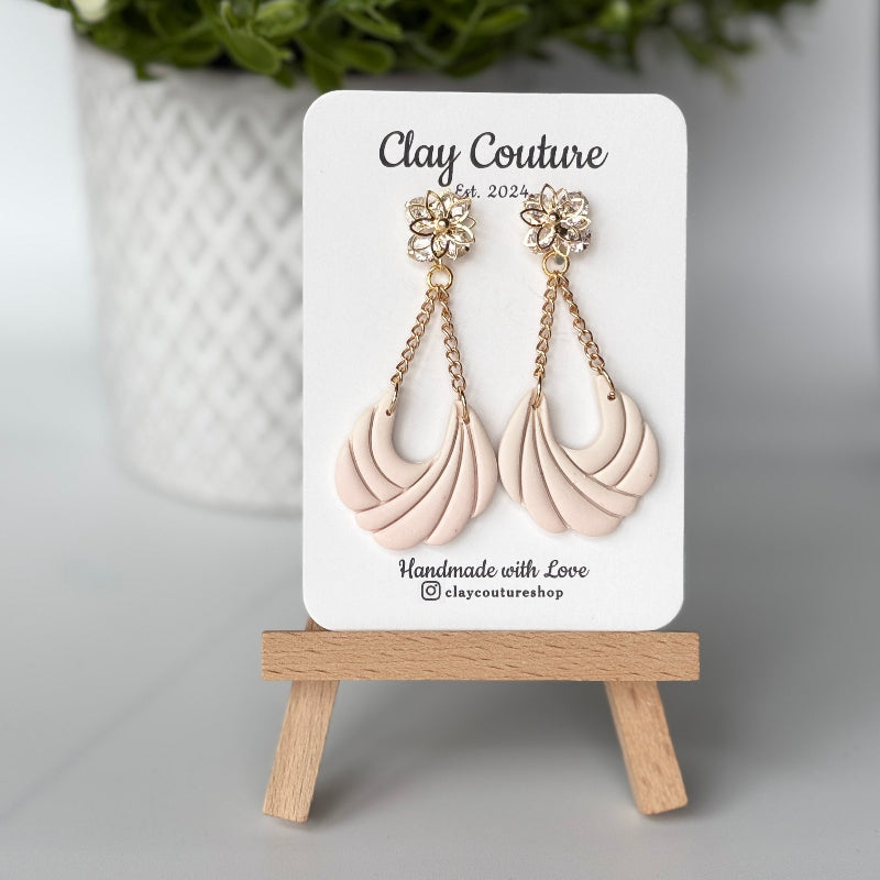 Pair of champaigne earrings on a 'Clay Couture' branded card with a wooden stand.