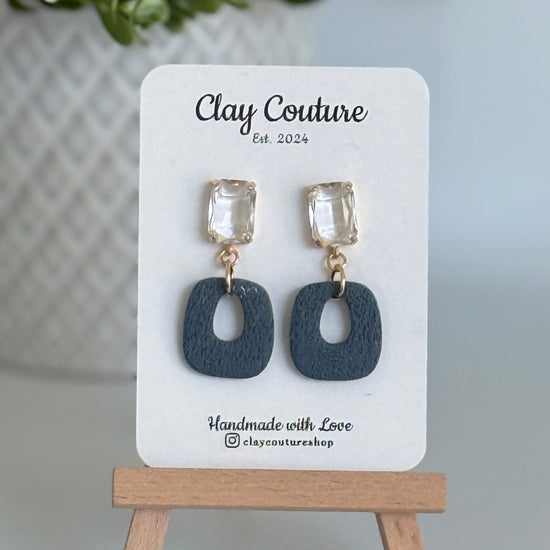 Plu polymer clay earrings with a crystal stud on a 'Clay Couture' branded card with a wooden standSlate Blue