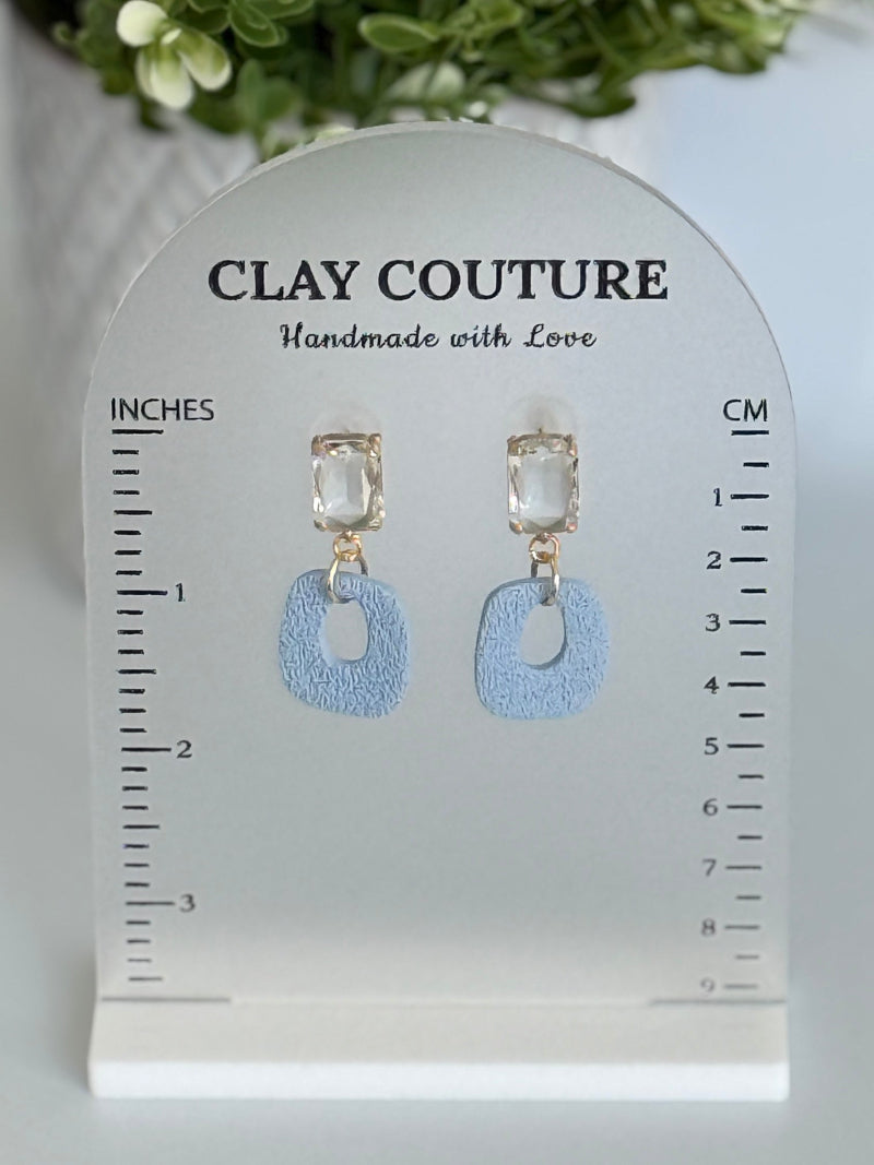Dusty Blue polymer clay earrings with a crystal stud on a 'Clay Couture' branded size stand