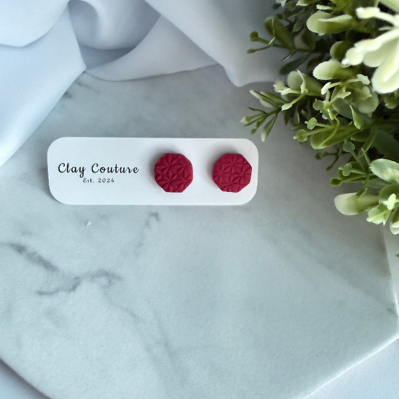 Red textured earrings on a Clay Couture card with greenery in the background