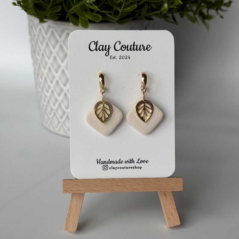 Polymer clay  earriings in Irish Creme color with and gold huggies brass charms on a 'Clay Couture' branded card with a plant in the background.
