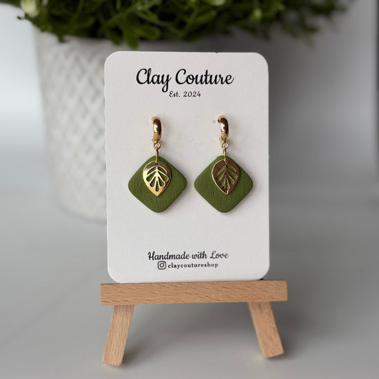 Polymer clay  earrings in Olive Grove color with and gold huggies brass charms on a 'Clay Couture' branded card with a plant in the background.