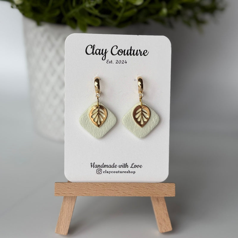 Polymer clay  earrings in Sage Mist color with and gold huggies brass charms on a 'Clay Couture' branded card with a plant in the background.
