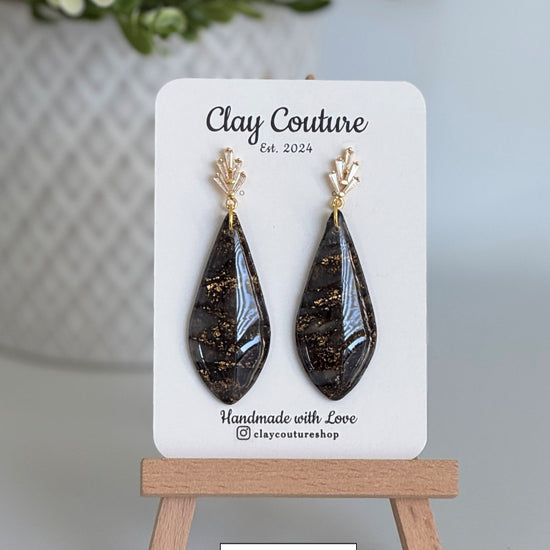 Black teardrop earrings on a 'Clay Couture' branded card with a wooden stand.