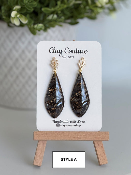 Black teardrop earrings on a 'Clay Couture' branded card with a wooden stand.