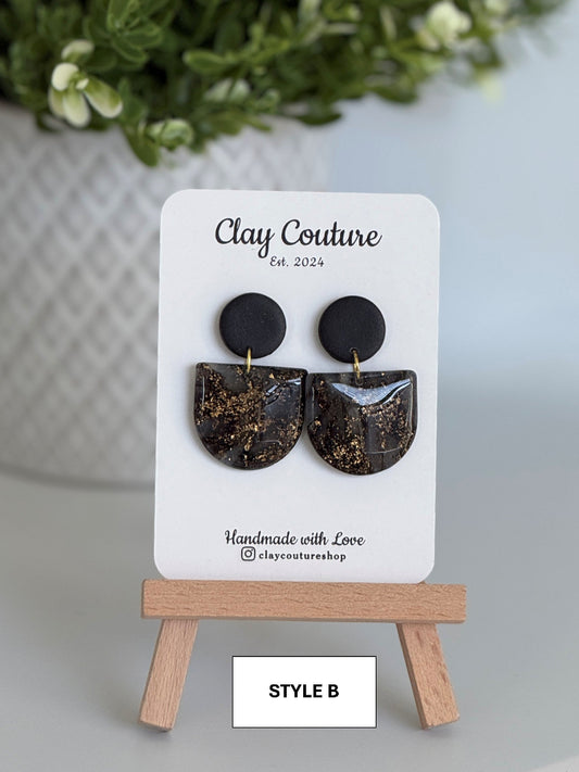 Black circular earrings on a 'Clay Couture' branded card with a wooden stand.