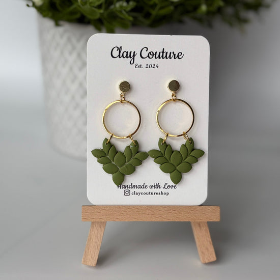 Pair of polymer clay earrings in Olive Grove on Clay Couture branded card on a wooden stand