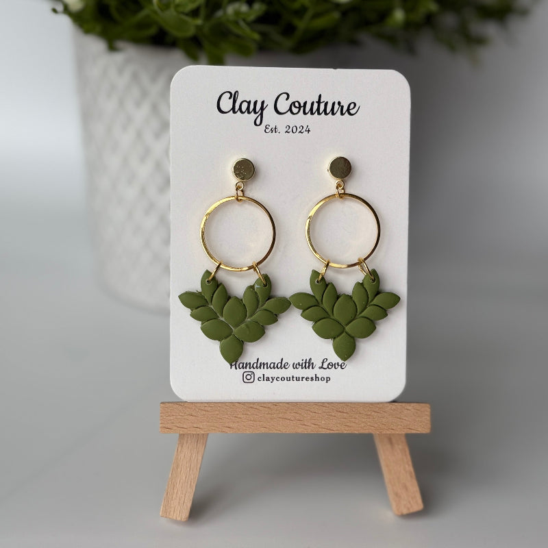 Pair of polymer clay earrings in Olive Grove on Clay Couture branded card on a wooden stand