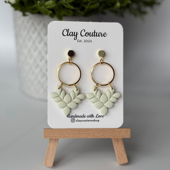 Pair of polymer clay earrings in Sage Mist on Clay Couture branded card on a wooden stand