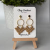 Pair of polymer clay earrings in warm sandstone on Clay Couture branded card on a wooden stand