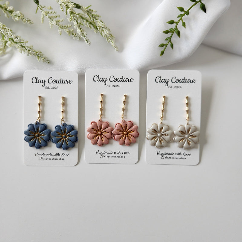 Three pairs of clay flower earrings on 'Clay Couture' cards with a white background.
