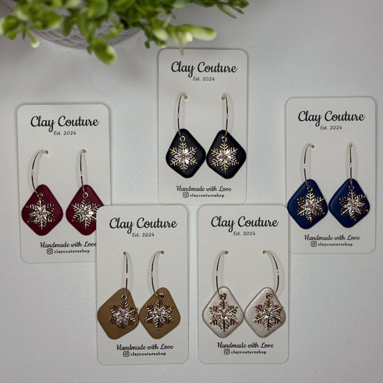 Set of snowflake-themed earrings on 'Clay Couture' cards against a white background.
