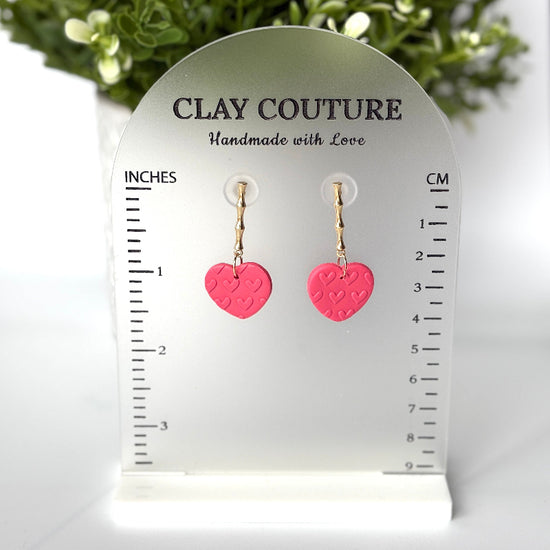 Pink heart-shaped earrings on a Clay Couture size stand