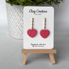 Heart-shaped earrings in Blush Rose color on a 'Clay Couture' branded card with a wooden stand.