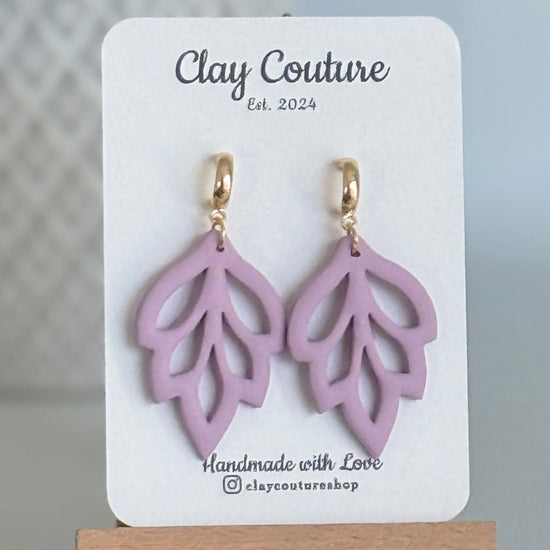 Embossed leaf design  earrings in Mauve color with gold plated hoops on a 'Clay Couture' branded card with a plant in the background.