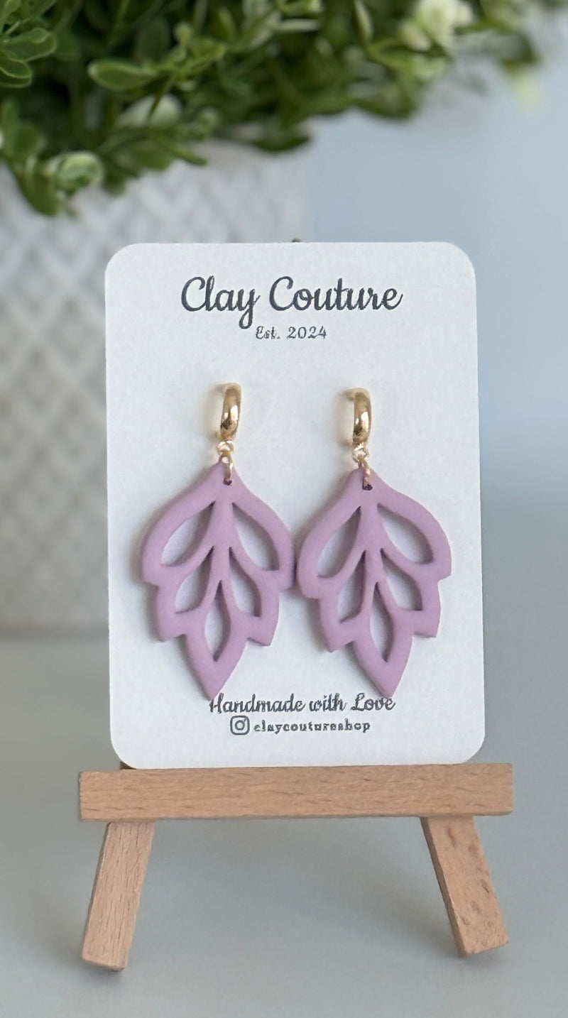 Embossed leaf design  earrings in Mauve color with gold plated hoops on a 'Clay Couture' branded card with a plant in the background.