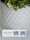Dusty Blue color Polymer Clay bow earrings on a Clay Couture card with a white textured background