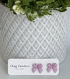 Mauve color Polymer Clay bow earrings on a Clay Couture card with a white textured background