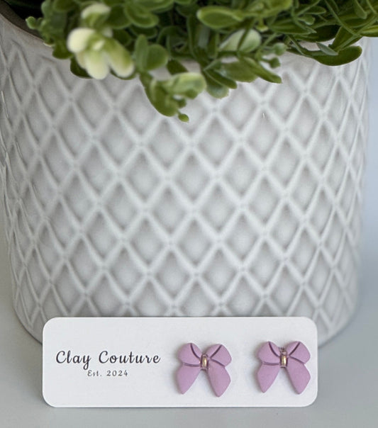 Mauve color Polymer Clay bow earrings on a Clay Couture card with a white textured background