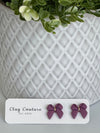 Plum color Polymer Clay bow earrings on a Clay Couture card with a white textured background
