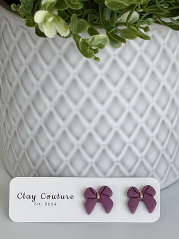 Plum color Polymer Clay bow earrings on a Clay Couture card with a white textured background