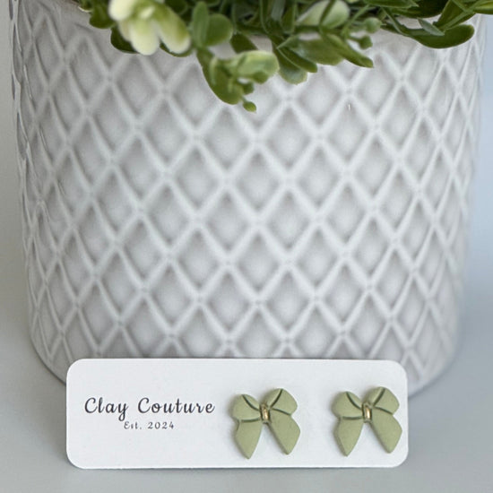 Sage color Polymer Clay bow earrings on a Clay Couture card with a white textured background