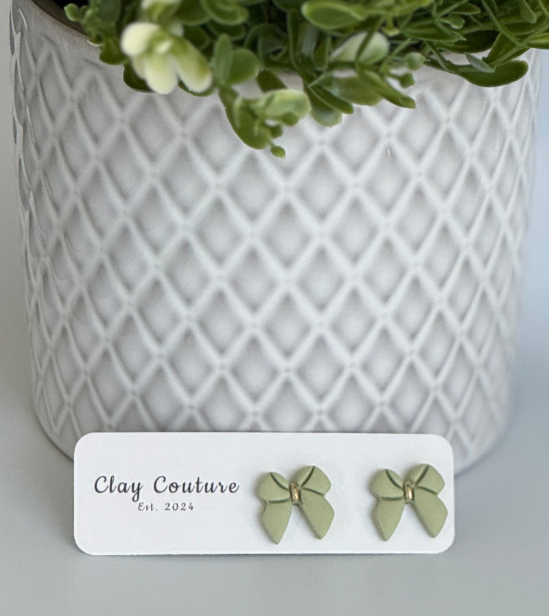 Sage color Polymer Clay bow earrings on a Clay Couture card with a white textured background