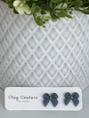 Slate Blue color Polymer Clay bow earrings on a Clay Couture card with a white textured background