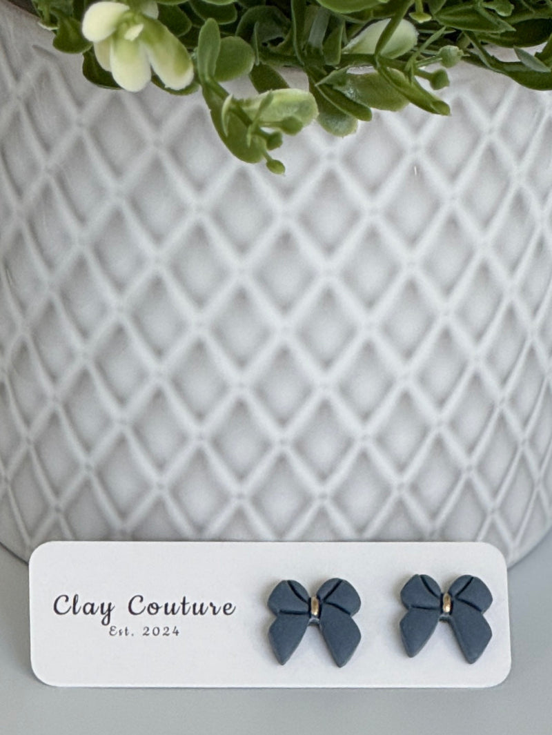 Slate Blue color Polymer Clay bow earrings on a Clay Couture card with a white textured background