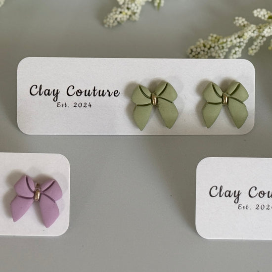 Set of bow shaped earrings on branded cards with a neutral background
