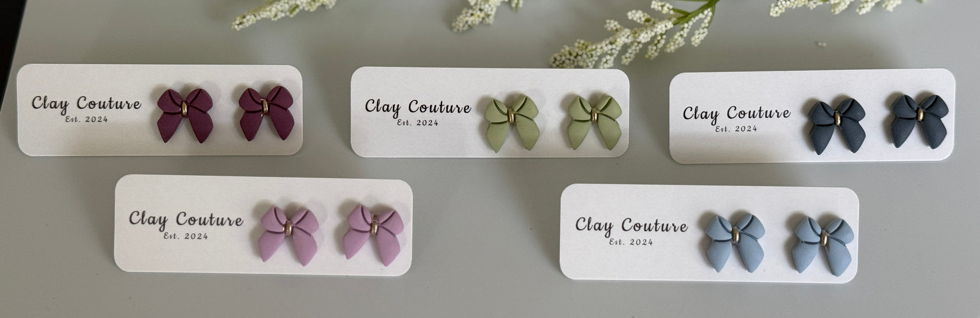 Set of bow shaped earrings on branded cards with a neutral background
