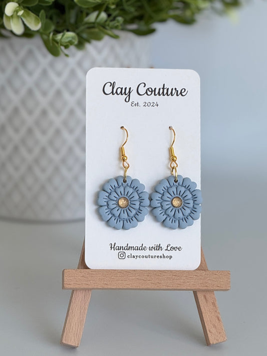 Dusty Blue flower earrings on a Clay Couture branded card with a wooden stand.