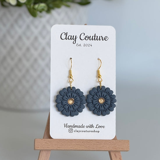 Slate Blue flower earrings on a Clay Couture branded card with a wooden stand.