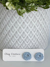 Dusty Blue Polymer Clay knot earrings on a Clay Couture card with a potted plant in the background