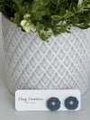 Slate Grey Polymer Clay knot earrings on a Clay Couture card with a potted plant in the backgroud.