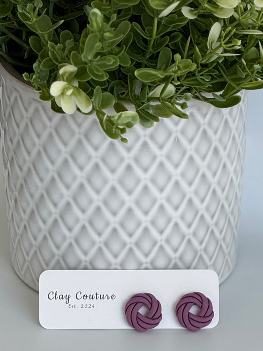 Plum Polymer Clay knot earrings on a Clay Couture card with a potted plant in the background
