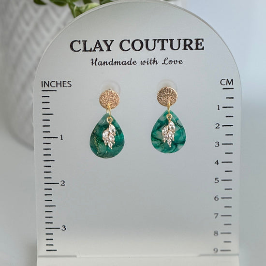 Emerald green polymer clay  earrings  with a resin finish and gold accents on a Clay Couture branded measuring stand showing the length of the earrings