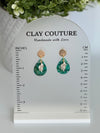 Emerald green polymer clay  earrings  with a resin finish and gold accents on a Clay Couture branded measuring stand showing the length of the earrings