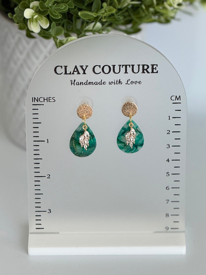 Emerald green polymer clay  earrings  with a resin finish and gold accents on a Clay Couture branded measuring stand showing the length of the earrings